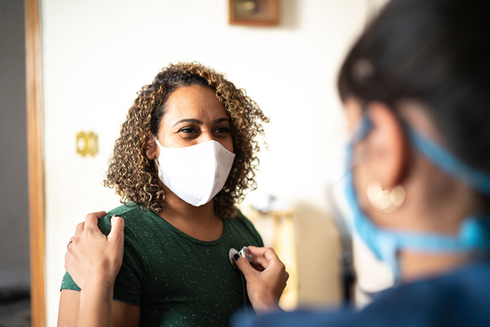 masked doctor listens to masked patient's heart beat