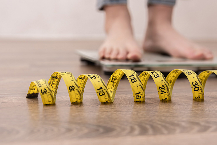 person standing on a scale with tape measure in the foreground
