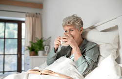 Senior woman in bed with a book, sipping from a mug