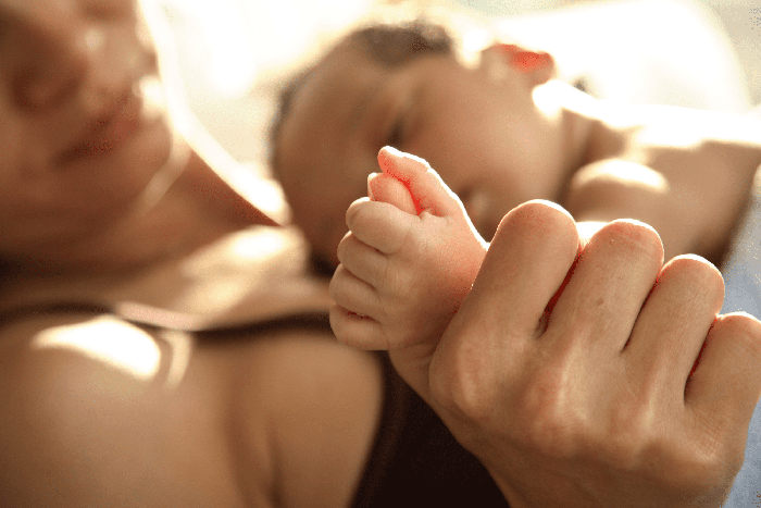 newborn baby's hand is wrapped around mom's thumb