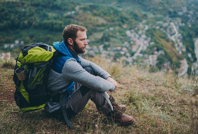 male hiker sits atop mountain in deep thought