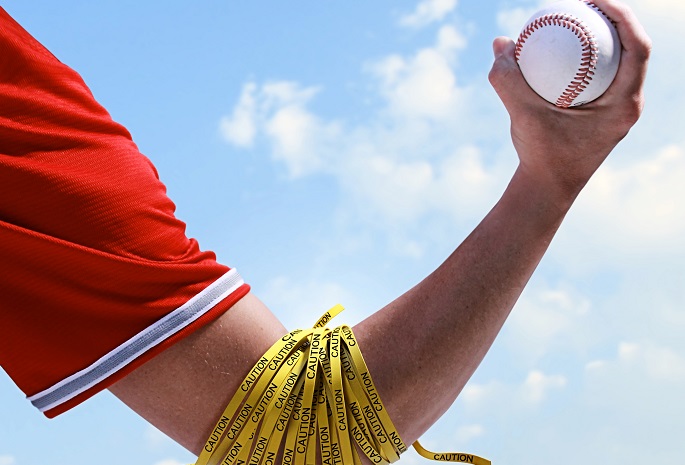 arm of pitcher holding baseball with caution tape around elbow