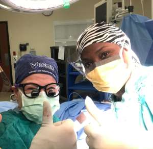 Vicki Teodorescu and Kenya Thomas in surgical scrubs giving a thumbs up from the operating room