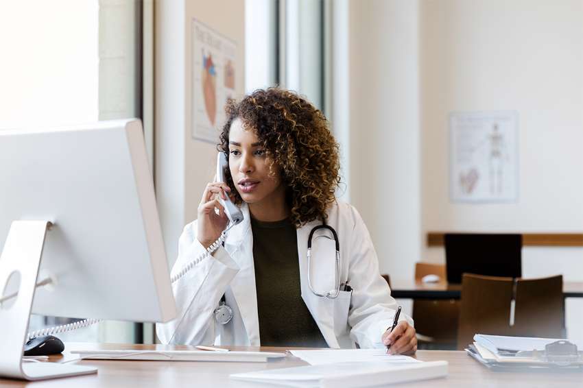 doctor sitting at a computer taking notes while talking on the phone