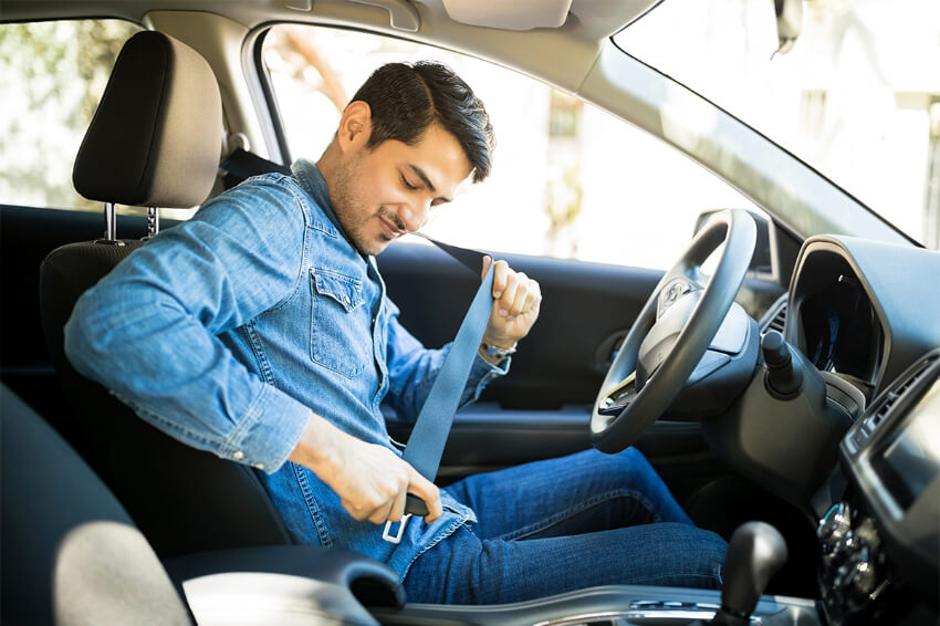 man sitting in driver's seat fastening his seat belt