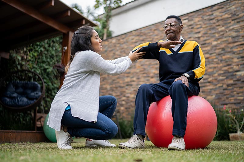woman helping man exercise sitting on a pilates ball